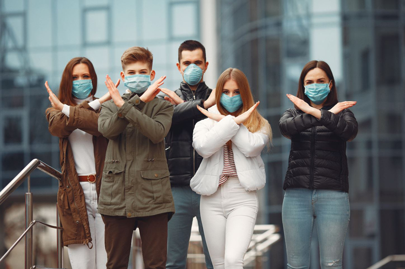 Crowd of people wearing surgical masks, crossing their arms in an X shape
