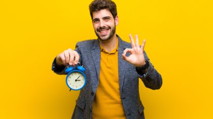 young handsome man with an alarm clock against orange background